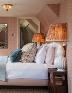 a bedroom with pink walls and white bedding, two lamps on either side of the bed