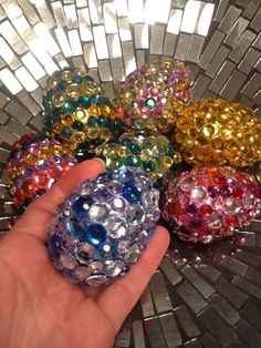 a hand is holding some colorful beads in front of a silver mosaic tile background with white squares