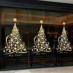 two christmas trees are in the window of a building with gold stars on each side