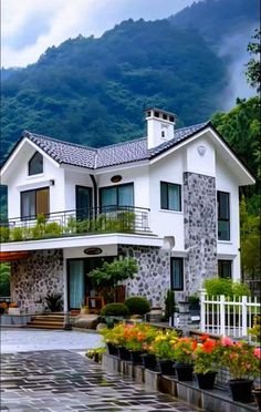 a large white house with lots of flowers in the front yard and mountains behind it