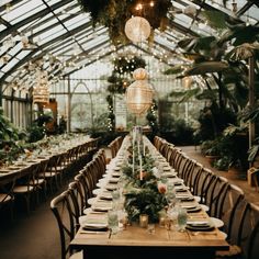 a long table set up with place settings and greenery for an event in a greenhouse