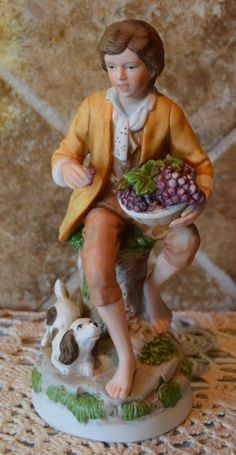 a figurine of a boy holding a plate with grapes and a dog on it