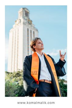 a man wearing an orange graduation stole standing in front of a tall building