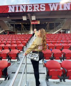 a woman is standing in the stands at a football game with her purse on her shoulder