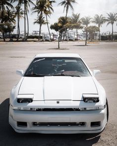 a white sports car parked in a parking lot with palm trees and buildings behind it