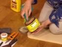 a woman is holding a jar of food on the floor with other items around her