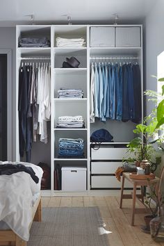 a white closet filled with clothes next to a bed