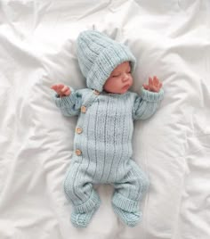 a baby is laying down wearing a blue knitted outfit with buttons and a hat