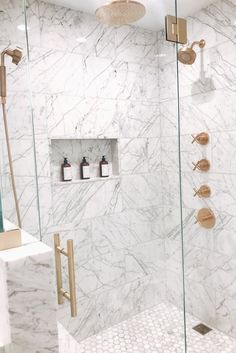 a white marble bathroom with gold fixtures and shower faucets on the wall next to it