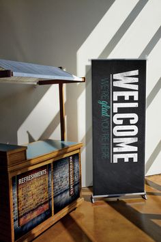 a welcome sign next to a wooden counter with an advertisement on it in the background