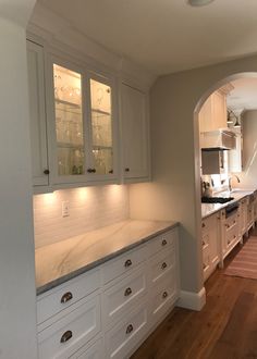 a kitchen with white cabinets and wood flooring in an archway leading to the dining room