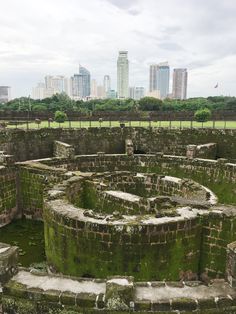 an old stone structure with moss growing on it in the middle of a city park