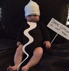 a baby sitting on a bed holding a sign that says same costume as last year