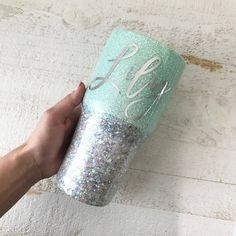 a hand holding a glittered cup with the word monogrammed in white letters