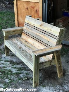 a wooden bench sitting in the grass next to a building and some wood planks