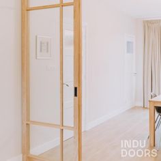 an open door leading to a dining room and living room with white walls, wood floors and beige drapes