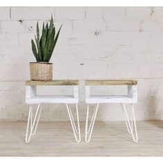 two white side tables with plants on them in front of a brick wall and wooden floor