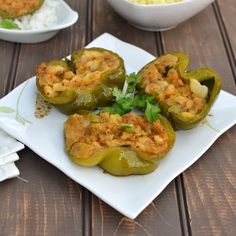 some stuffed peppers on a white plate with rice and garnishes in the background