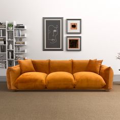 an orange couch sitting in front of a white wall with pictures on the wall behind it