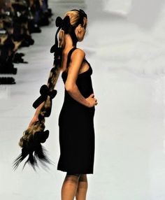 a woman in a black dress with long hair walking down the runway at a fashion show