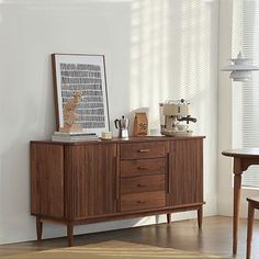 a wooden sideboard sitting next to a window in a living room with white walls