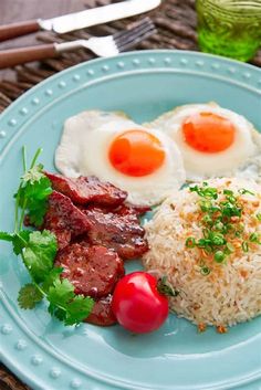 a blue plate topped with rice, meat and fried eggs next to tomato wedges