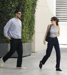 a man and woman are walking down the street with sunglasses on their heads, one is wearing black pants