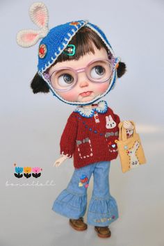 a doll with glasses and a knitted hat holding a stuffed animal in it's hand