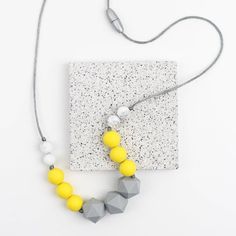 a necklace with yellow beads and grey hexagonals on a gray string next to a white square