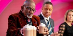 an older man holding two cups of hot chocolate milkshakes with whipped cream on them