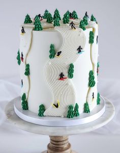 a white cake with green trees and skiers on the top is sitting on a pedestal