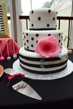 a three tiered cake with black and white stripes, polka dots and a pink flower