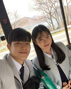 two people sitting on a bus with trees in the background