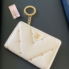 a white purse with a gold keychain attached to it and a tag hanging from the front