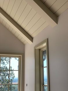 two windows in a room with white walls and wood trim on the ceiling, along with a window sill