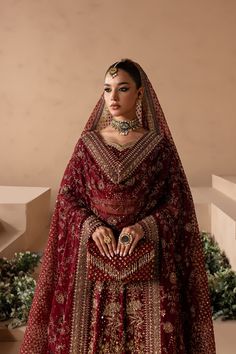 a woman in a red and gold bridal gown with jewelry on her head, standing next