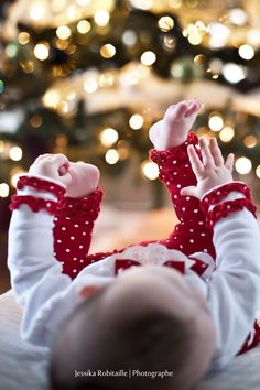 a baby laying on its back in front of a christmas tree with her hands up