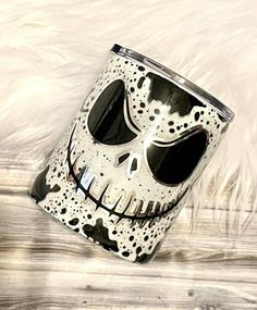 a black and white coffee mug with a skull face on it's side sitting on a wooden surface