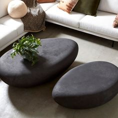 two black tables sitting on top of a white couch next to pillows and potted plant