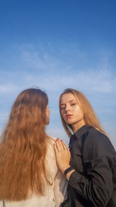 two women standing next to each other with their hands on their chests and looking at the sky