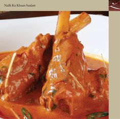 a close up of a plate of food with meat and sauce on the side that says nalli ka khaas saalahan shanks of baby lamb, braised in