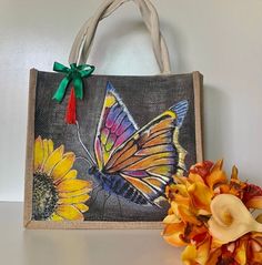 a bag with a butterfly painted on it next to a sunflower and a flower vase