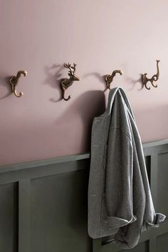 three coat hooks are mounted on the wall next to a towel rack with two coats hanging from it