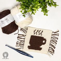 two crocheted coffee mugs on a table next to a plant