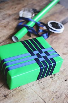 a green gift box with blue and black stripes next to a pair of scissors on a wooden table