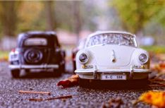 two toy cars are sitting on the ground next to each other in front of some leaves