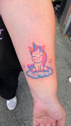 a small unicorn tattoo on the left inner arm and wrist, sitting on top of a cloud