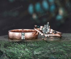 two gold wedding rings with green and white diamonds on top of a rock in front of a dark background