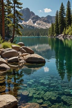 a lake surrounded by rocks and trees with mountains in the background