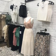 clothes on display in a clothing store with white brick wall and black and white tile floor